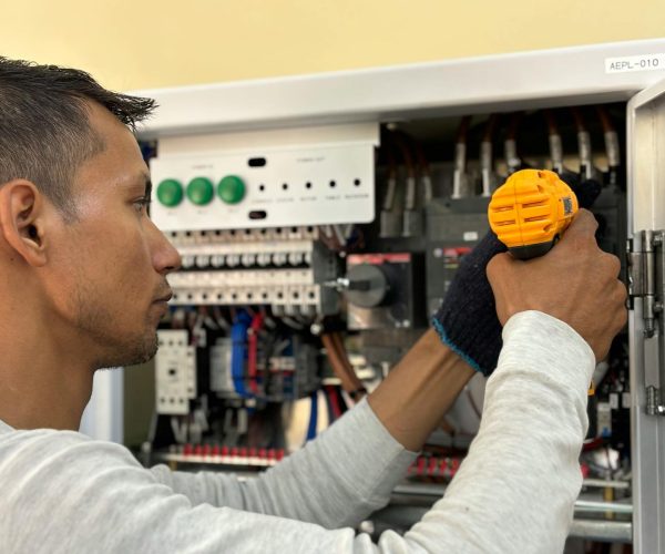 Skilled electrician using a drill to repair electrical equipment indoors. Focus on precision and safety.
