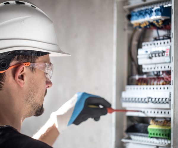 Man, an electrical technician working in a switchboard with fuses. Installation and connection of electrical equipment. Professional with tools in hand. concept of complex work, space for text. SSUCv3H4sIAAAAAAAEAI1Ry2rDMBC8F/oPRucYZMchdv+gh0LvoYe1tIlFFW3QoyWE/HslKyo6ld60M6vZnZ3b81PTsBmcEuyluaUq1krr4LwFr8hEmG8euEUj0dYISuXJKtA1OIMXi4EzRtAErRN8X0nmPPjg0KVhD0iAx1PUyOCvRN7okOumECsZf0SKvSNdNLJNxbgwJ+ZNOYFag0EKjhX+vvlD7NXIZDk5+b9gfnwU33BCI66rtcqyRY2QLR9yK/v89mjP9REgSEWV/y8SoFPDtlK6WCWUOVXfyC9rHuWboGC8TSuwYoNpogvMOoVxjJpY8AWci+2y4NUgEU9B52qOIb8aeKgyGTNLZbftu3EYdkPX7Uc+8h1nJWcSn0rWFnP0i4qUvVa4ShuwnostiGnfTv00tEOPuxYQx3bY81FwfpxG4PHw9x+hX0Y7sQIAAA==