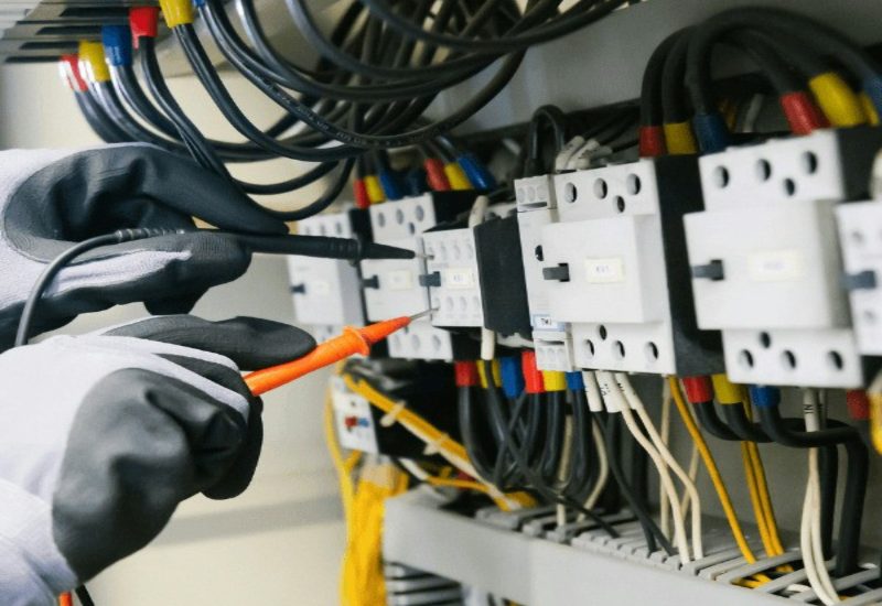 Electrician testing electrical panel with multimeter.